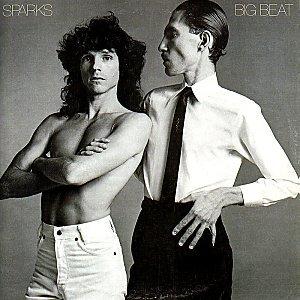 A black and white picture of two men. The man on the left is bare chested and wearing white jeans.. The man with the small moustache on  the right is posed and  wearing a white shirt and thin black tie and remarkable cheekbones.