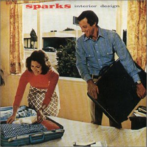 A 60s or 70s stock photograph of a man and a woman in a bedroom. The woman, on the left, is arranging clothes in an open suitcase on the bed. The man is standing on the right holding a closed suitcase. Through the window is another house with a car parked in front of it. Neither of the people have a small moustache.