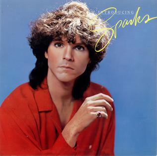 A picture of a man with curly hair wearing a red shirt on a blue background with the words 'Introducing Sparks' in the top right quadrant. The man with the small moustache is not present.