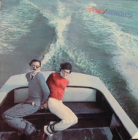 Two men bound and gagged in the back of a speedboat , its wake behind them. The man on the left has a small moustache, the one on the right does not.