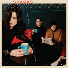 The sleeve for 'The Girl Is Crying In Her Latte' by Sparks. In the foreground a young woman with dark hair in a Veronica Lake style and dark clothing is sitting at a round table holding a blue mug of latte. She is crying and mascara is tricking down her face. In the background, the man with the small moustache and the man with the floppy hair are sitting on a red couch. The man with the small moustache is holding a blue mug and the man with the floppy hair is holding a newspaper.